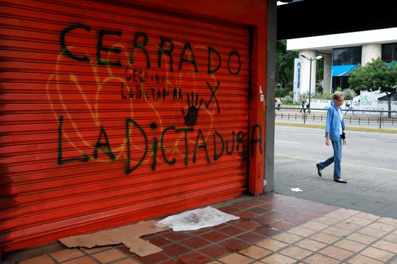 A woman walks on a street close to a graffiti that reads 