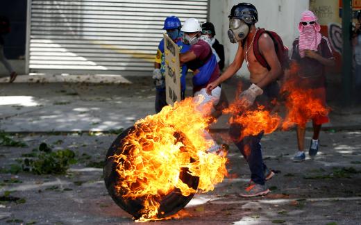 Demonstrators use a tire on fire to block a street at a rally during a strike called to protest against Venezuelan President Nicolas Maduro