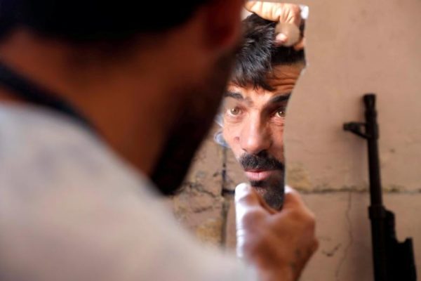 A fighter of Syrian Democratic Forces fixes his hair using a broken mirror at the frontline. REUTERS/Erik De Castro